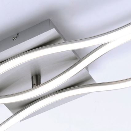 Svietidlo s dvoma vlnovitými LED pásikmi je pripevnené k stropu. Strieborná kovová konštrukcia drží svetelné prvky. Celok pôsobí moderným dojmom.