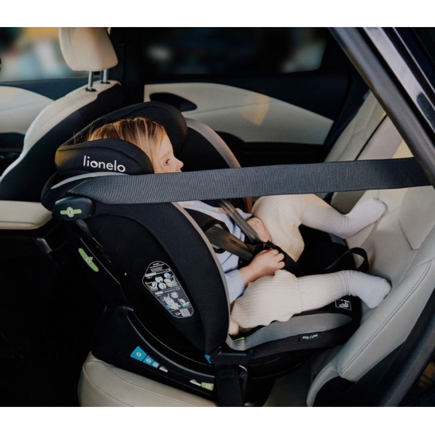 Dieťa sedí v čiernej autosedačke Lionelo v aute. Autosedačka je pripevnená bezpečnostným pásom. Dieťa je pripútané vnútornými pásmi autosedačky.
