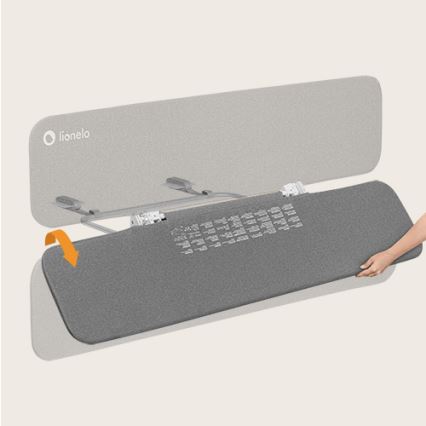 Šedá podložka sa pripája k kovovému rámu. Ruka pripevňuje podložku k rámu. Značka Lionelo je na hornej časti.