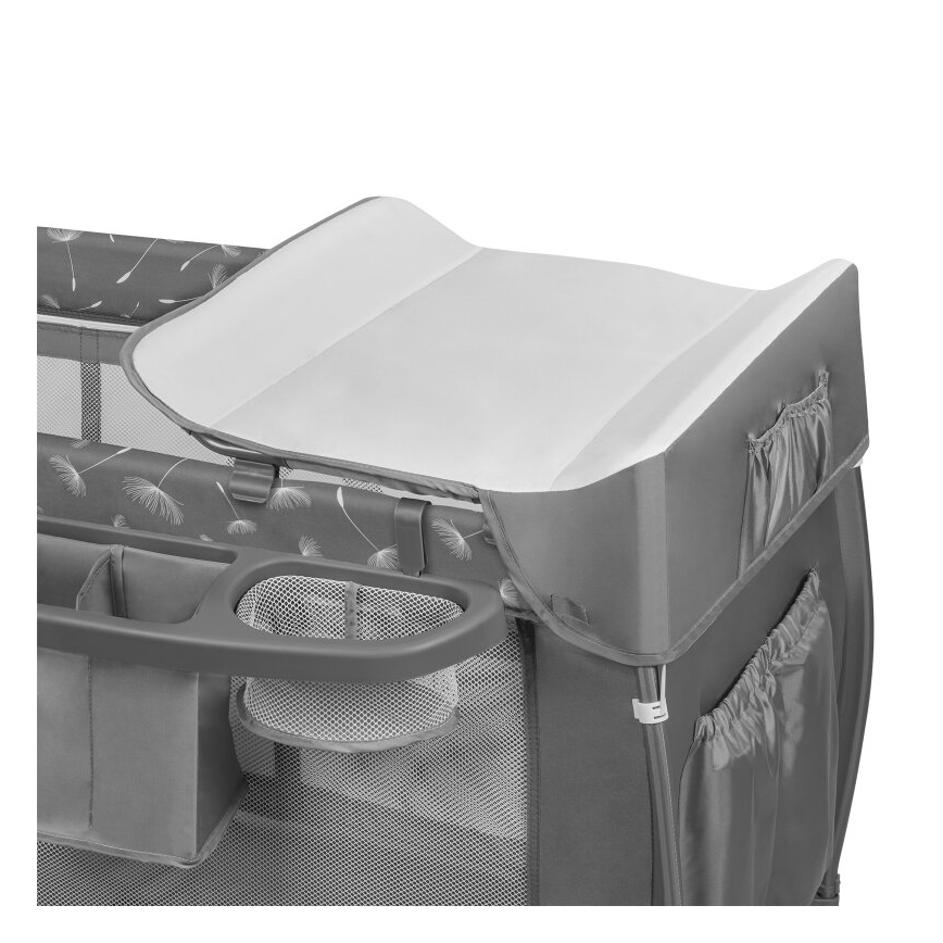 Prebaľovacia podložka je umiestnená na vrchu prenosnej postieľky. Postieľka je sivá s obrázkami púpavy, obsahuje bočné vrecká a odkladacie priestory.