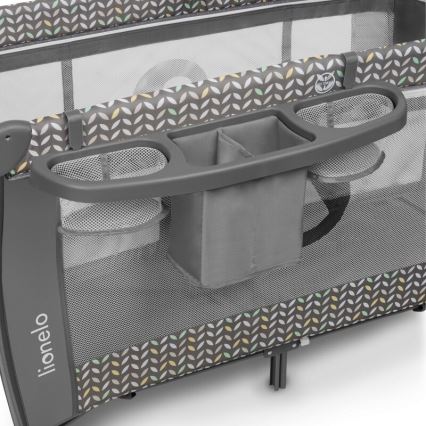 Cestovná postieľka Lionelo obsahuje odkladací priestor s viacerými priehradkami a sieťovanými vreckami. Je sivá s dekoratívnym vzorom listov v pastelových farbách. Postieľka je rozložená.
