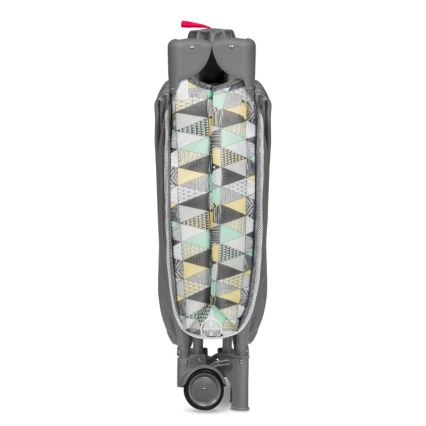 Prebaľovacia posteľ je zložená. Má sivý rám a vnútornú časť s geometrickým vzorom v pastelových farbách (mint, žltá, šedá). Je na kolieskach.