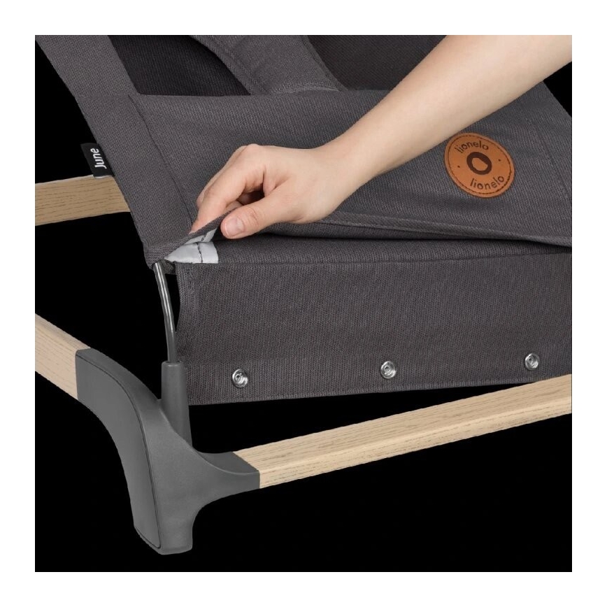 Ruka pripája tmavosivú látkovú striešku k detskej lehátku s drevenými a tmavosivými plastovými prvkami. Lehátko má značku Lionelo.