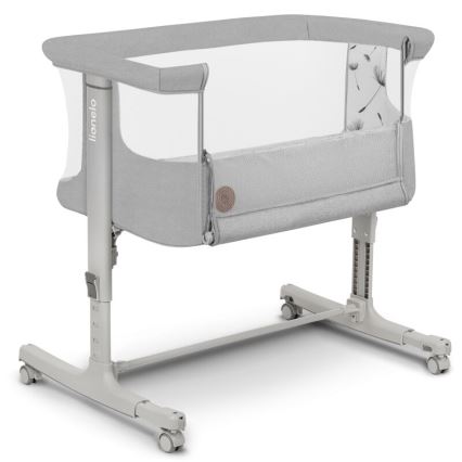 Detská postieľka na kolieskach stojí na svetlom podklade. Je sivá s priehľadnou sieťovinou a detailom s púpavou. Výrobca je Lionelo.