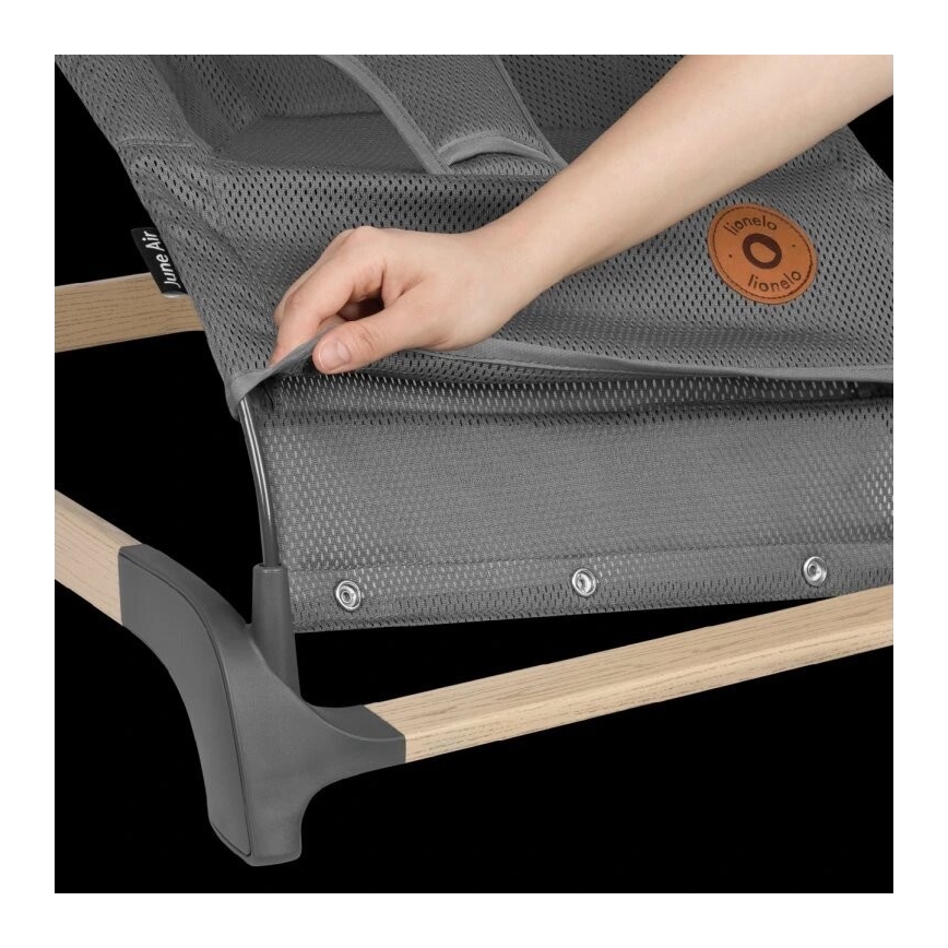 Ruka napína sivú sieťovinu lehátka s drevenými a šedými časťami konštrukcie. Na sieťovine je viditeľné logo „Lionelo“. Lehátko je položené na tmavom pozadí.