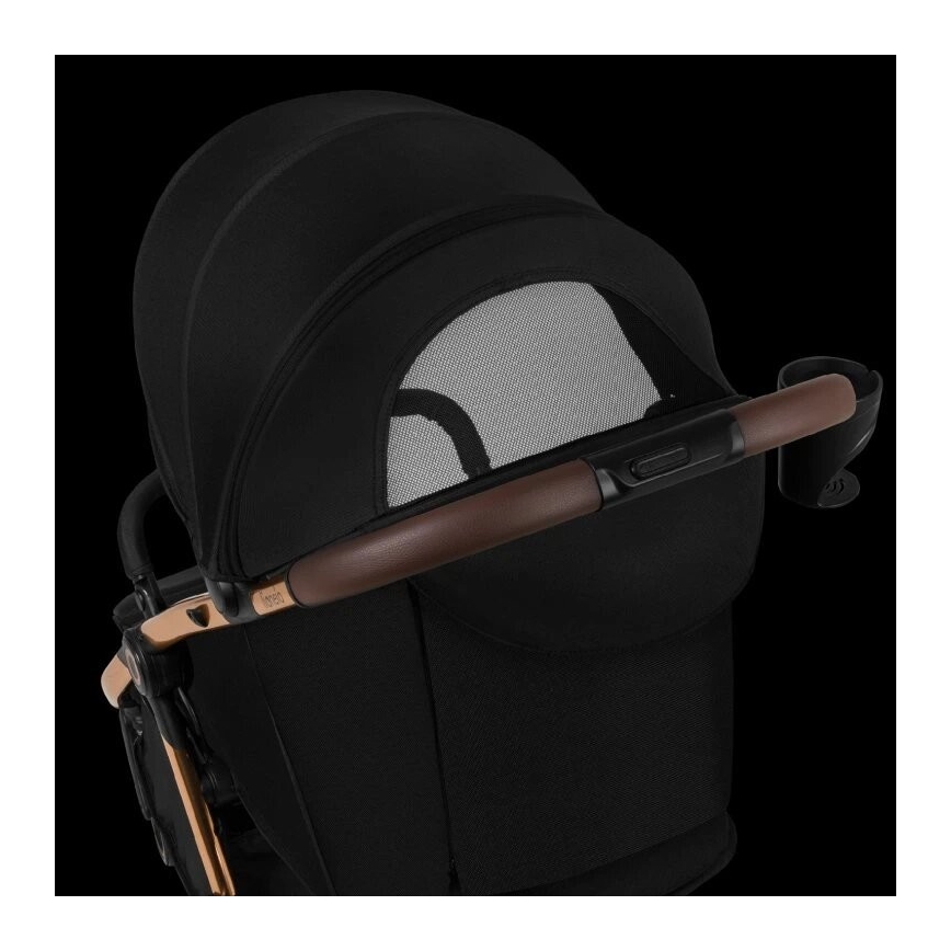 Kočík má rozopnutú čiernu striešku s prieduchom zo sieťoviny. Hnedá rukoväť je pripevnená k strieške. Konštrukcia kočíka je čiastočne viditeľná, má medené detaily.