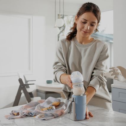 Žena v svetrom svetri naleje mlieko do detskej fľaše, ktorú následne vloží do termotašky značky Hemel. Scéna sa odohráva v kuchyni.