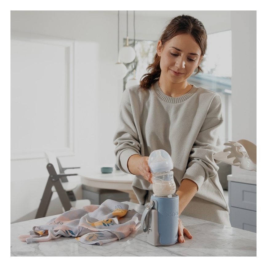 Žena v svetrom svetri naleje mlieko do detskej fľaše, ktorú následne vloží do termotašky značky Hemel. Scéna sa odohráva v kuchyni.