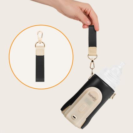 Ruka pripája popruh k fľaši v termotaške lianelo. Taška je béžová s čiernym puzdrom a obsahuje fľašu s cumlíkom. Popruh je čierny s béžovými detailmi a karabínkou.