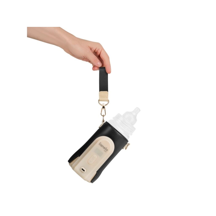 Ruka drží ohrievač fľaštičiek Liomelio v čiernom puzdre s popruhom. Fľaštička s cumlíkom je vložená do puzdra. Biely podklad.