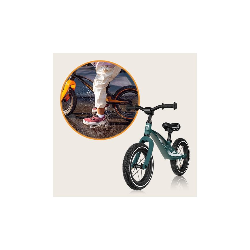 Detské odrážadlové kolo tmavozelenej farby s čiernymi kolesami stojí na bielom pozadí. V pozadí je zobrazené dieťa, ktoré sa na podobnom odrážadle prechádza vonku po mokrej ceste.