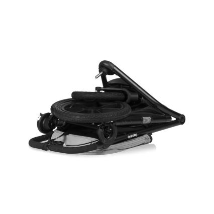 Kočík je zložený, pričom kolesá sú zložene na jeho ráme. Rám je čierny, sedacia časť svetlosivá. Na ráme je viditeľné logo „Tutetelo“. Kočík je umiestnený na bielom pozadí.