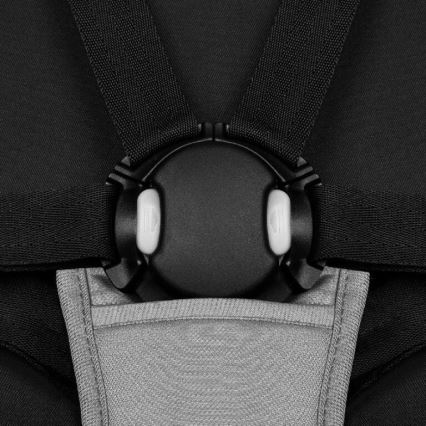 Pásy na detskej autosedačke sa spínajú v kruhovom mechanizme s dvoma tlačidlami. Mechanizmus je čierny, pásy čierne, pod ním je svetlosivá podložka.