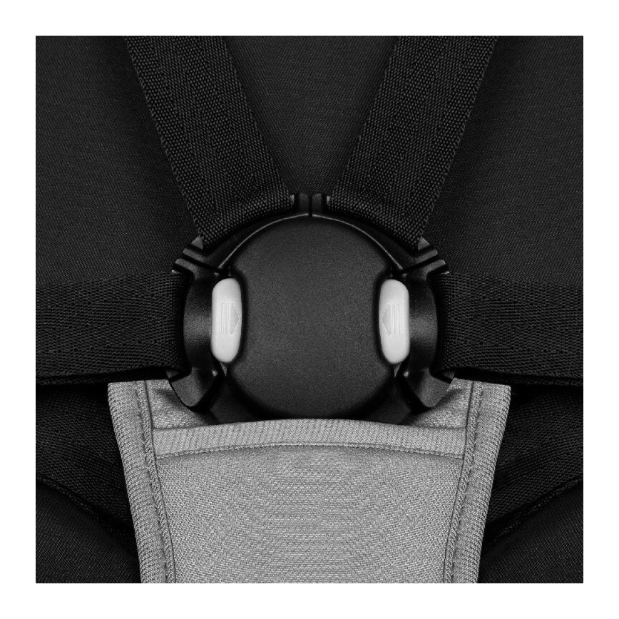 Pásy na detskej autosedačke sa spínajú v kruhovom mechanizme s dvoma tlačidlami. Mechanizmus je čierny, pásy čierne, pod ním je svetlosivá podložka.