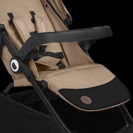 Kočík je sklopený do polohy na ležanie. Má béžové čalúnenie a čierne plastové prvky, vrátane opierky rúk. Je zobrazený na čiernom pozadí.