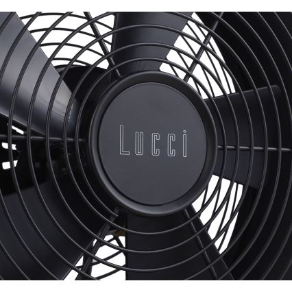 Čierny ventilátor značky Lucci s kovovými lopatkami roztáča svoje lopatky. Viditeľná je stredová časť s logom.