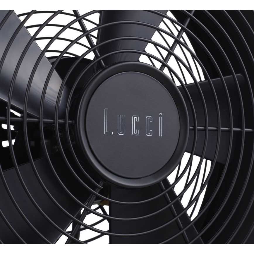 Čierny ventilátor značky Lucci s kovovými lopatkami roztáča svoje lopatky. Viditeľná je stredová časť s logom.