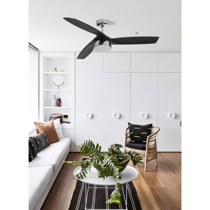 Trojlistový stropný ventilátor s čiernymi lopatkami a strieborným stredom sa otáča v modernej obývacej izbe s bielym nábytkom a drevenou podlahou.