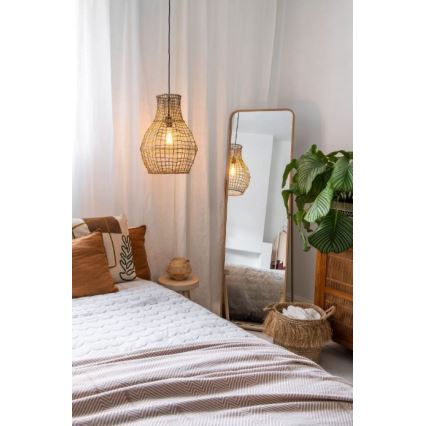 Pletacia lampa visí nad posteľou s prehozom. Lampa osvetľuje izbu s vysokým zrkadlom a rastlinou v kvetináči.
