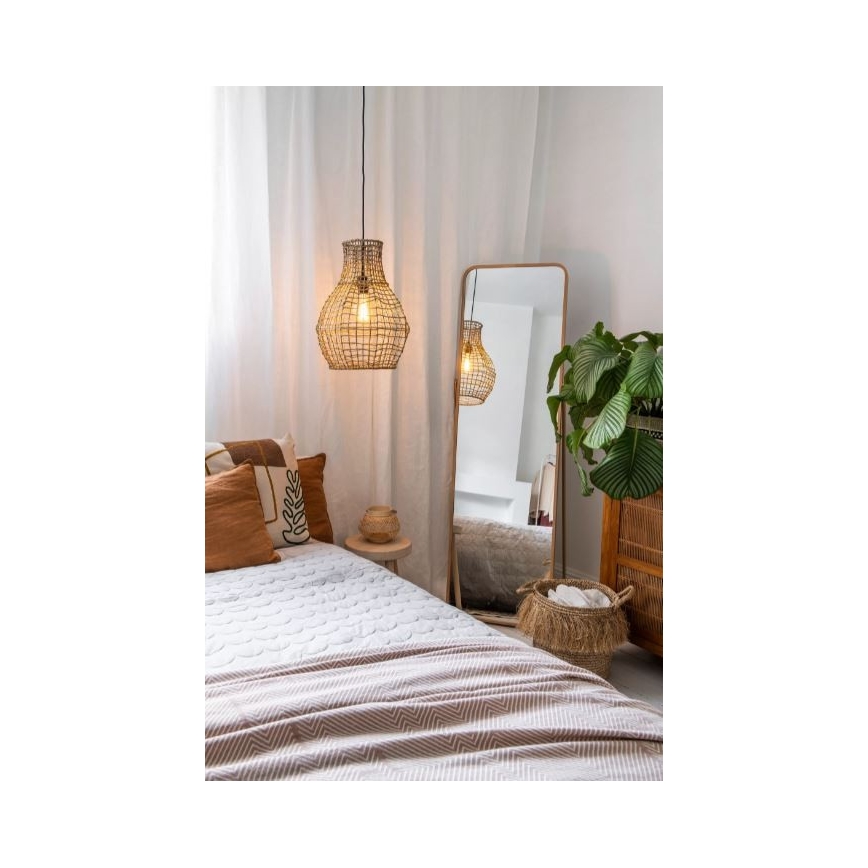Pletacia lampa visí nad posteľou s prehozom. Lampa osvetľuje izbu s vysokým zrkadlom a rastlinou v kvetináči.