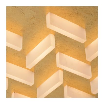 Svietidlo svieti na zlatom strope. Množstvo obdĺžnikových prvkov svietidla je prekrytých a vytvára geometrický vzor. Prvky sú priesvitné a vyžarujú svetlo.