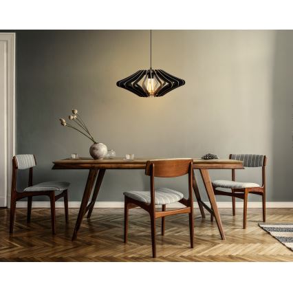Moderné drevené svietidlo visí nad dreveným jedálenským stolom so štyrmi stoličkami v jedálni. Svietidlo má čiernu farbu a tvar kvetu.