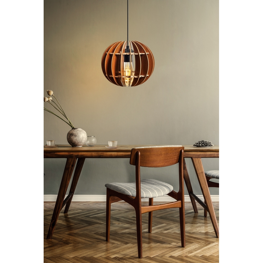 Drevená lampa visí nad jedálenským stolom. Lampa je guľatá, s drevenými lamelami. Stôl je drevený, s drevenými stoličkami.