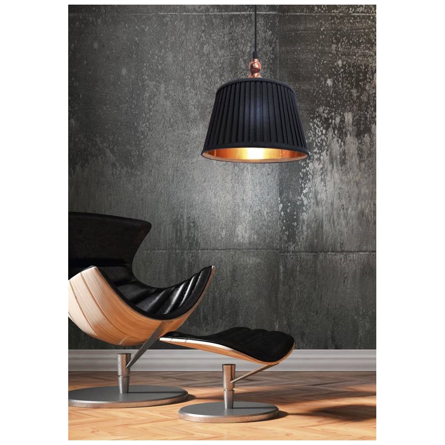 Čierna závesná lampa s medeným detailom visí nad čiernym koženým kreslom a podnožkou s drevenými prvkami. Kreslo a podnožka stoja na drevenej podlahe pred betónovou stenou.