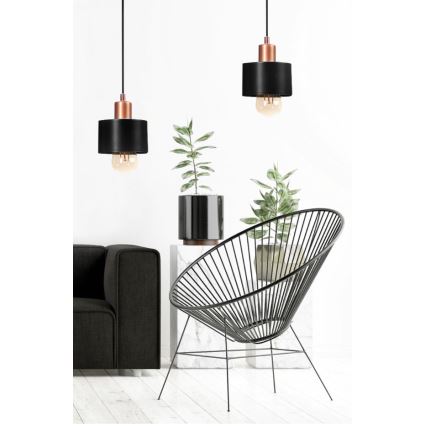 Dve čierne závesné lampy s medenými detailmi visia nad sedačkou a stolíkom s kvetináčmi v modernom interiéri.