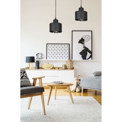 Dve čierne závesné lampy svietia v obývacej izbe. Moderný nábytok a dekorácie v čierno-bielej farebnej schéme tvoria prostredie.