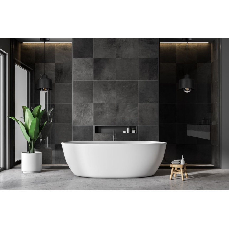 Biela voľne stojaca vaňa stojí v modernej kúpeľni s tmavosivou dlažbou. Dve čierne závesné svietidlá osvetľujú priestor. V kúpeľni je tiež zelená rastlina v bielom kvetináči a drevený stolík.