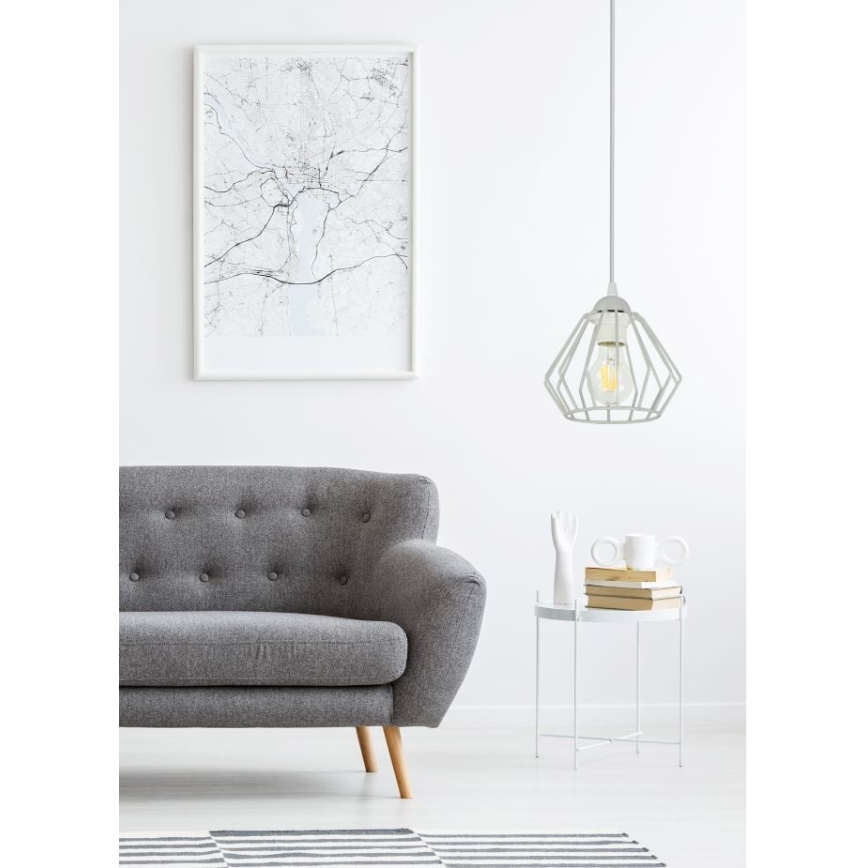 Biela závesná lampa s geometrickým tienidlom svieti v obývacej izbe. Šedá pohovka stojí oproti konferenčnému stolíku s knihami a dekórom. Na stene visí obraz.