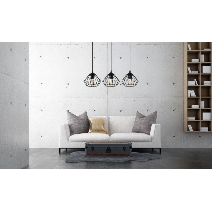 Tri čierne geometrické závesné svietidlá visia nad bielou sedačkou v modernom interiéri s betónovou stenou a knižnicou.
