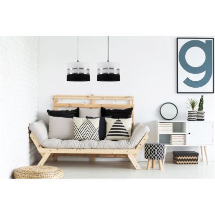 Dve závesné lampy s bielym tienidlom a čiernym a strieborným prúžkom visia nad drevenou pohovkou s vankúšmi v obývacej izbe.