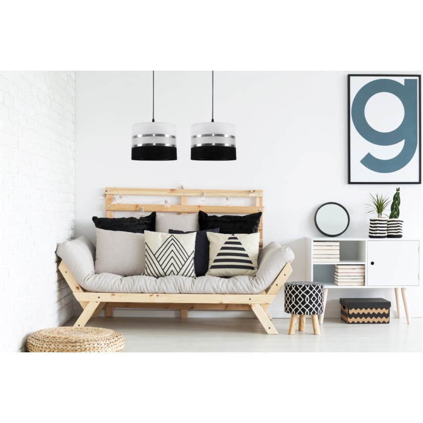 Dve závesné lampy s bielym tienidlom a čiernym a strieborným prúžkom visia nad drevenou pohovkou s vankúšmi v obývacej izbe.