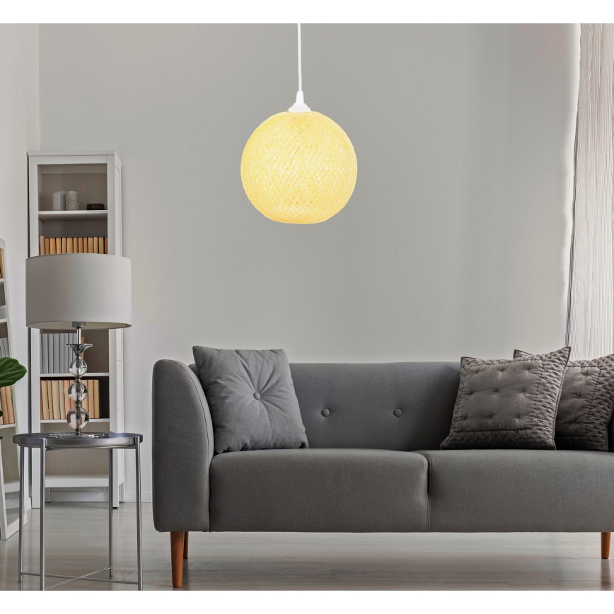 Guľové textilné svietidlo visí v obývacej izbe nad sivou pohovkou s vankúšmi. Svietidlo je svetložltej farby.