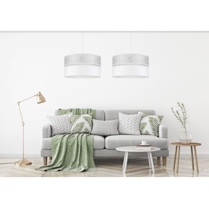 Dve dvojité závesné svietidlá s bielym a sivým tienidlom visia nad sivou sedačkou s vankúšmi a svetlozelenou dekou v svetlej obývacej izbe.