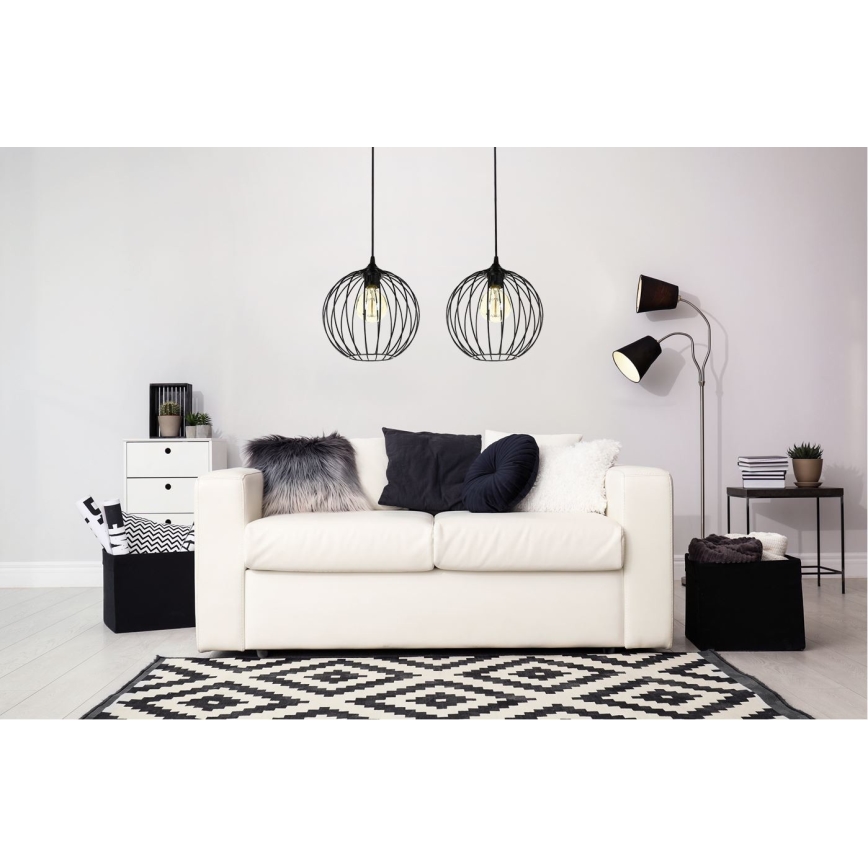 Dve čierne závesné svietidlá s kovovou konštrukciou v tvare gule visia nad bielym gaučom v obývacej izbe. Izba obsahuje aj stolík, koberec a ďalšie dekoračné prvky.