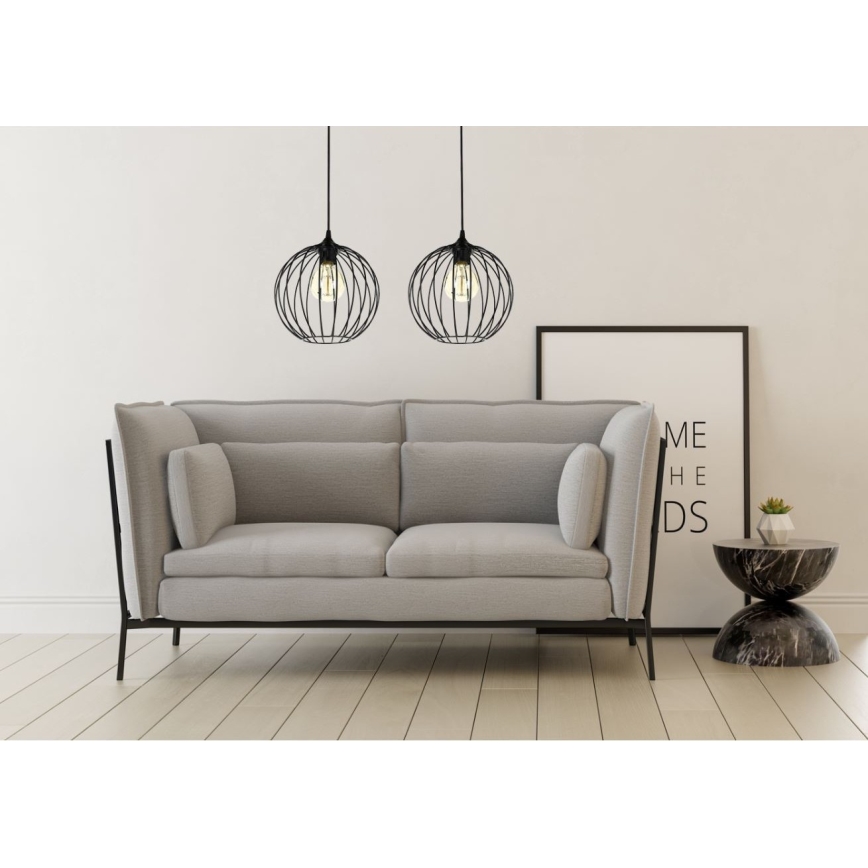 Dve čierne kovové závesné lampy s guľovým tienidlom visia nad svetlosivou pohovkou. V pozadí je rám obrazu s textom „ME HE DS“.