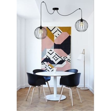 Dve závesné lampy s kovovými tienidlami visia nad jedálenským stolom. Lampa je súčasťou interiéru s drevenou podlahou a abstraktným obrazom na stene.