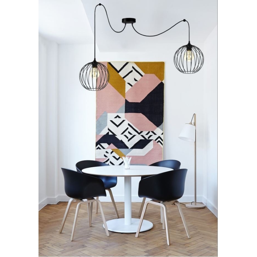 Dve závesné lampy s kovovými tienidlami visia nad jedálenským stolom. Lampa je súčasťou interiéru s drevenou podlahou a abstraktným obrazom na stene.