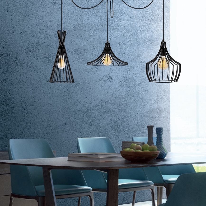 Tri čierne kovové závesné lampy svietia nad jedálenským stolom. Lampa svietidlá sú umiestnené v modernom interiéri s modrými stenami a svetlomodrými stoličkami. Na stole sú ovocie a knihy.
