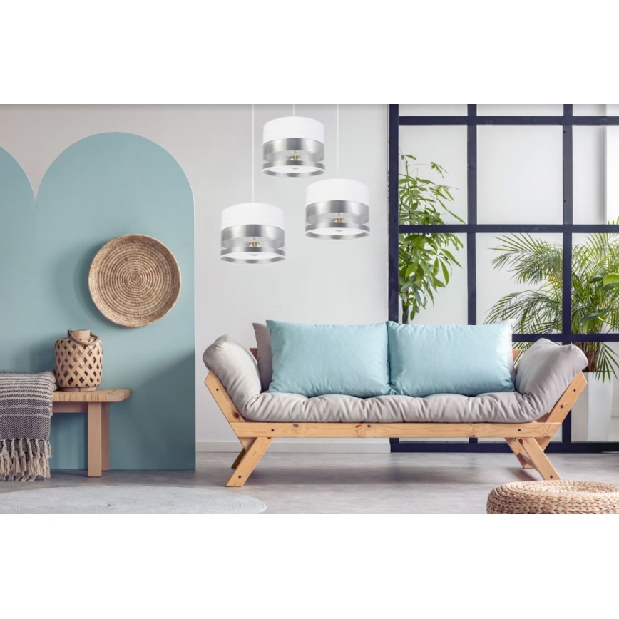 Tri visiace svietidlá s bielym a strieborným tienidlom osvetľujú obývaciu izbu. Svietidlá sú umiestnené nad drevenou pohovkou s bledomodrými vankúšmi. Pohovka stojí v priestore s rastlinami a svetlomodrými stenami.