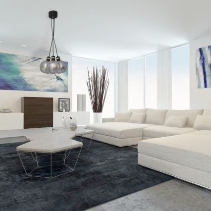 Trojramenné závesné svietidlo s dymovými sklenenými tienidlami visí nad modernou, bielou sedačkou v obývacej izbe. Sedačka je umiestnená na tmavosivej koberec.