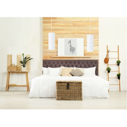 Dve valcovité závesné lampy visia nad manželskou posteľou v spálni. Posteľ má hnedé čelo a je prezlečená bielou posteľnou bielizňou. Na stene za posteľou je drevená obkladacia stena a obraz zobrazujúci žirafu.