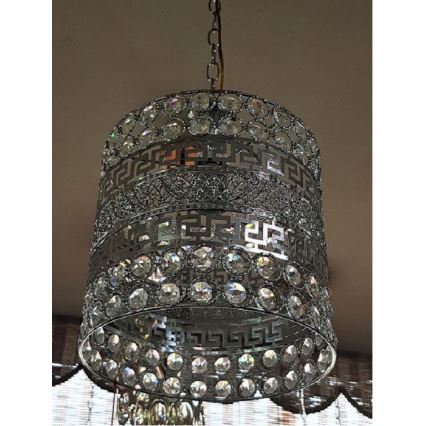 Stropné svietidlo visí zo stropu. Svietidlo je valcového tvaru, kovové, striebornej farby, zdobené krištáľmi a gréckym vzorom. Svietidlo je osvetlené.