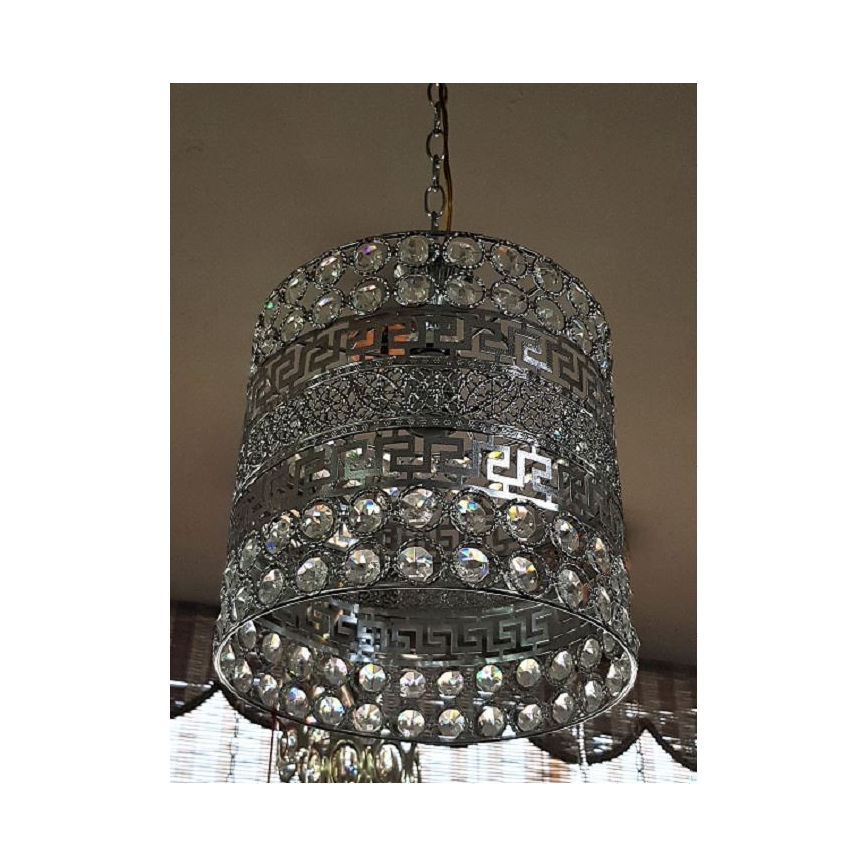 Stropné svietidlo visí zo stropu. Svietidlo je valcového tvaru, kovové, striebornej farby, zdobené krištáľmi a gréckym vzorom. Svietidlo je osvetlené.