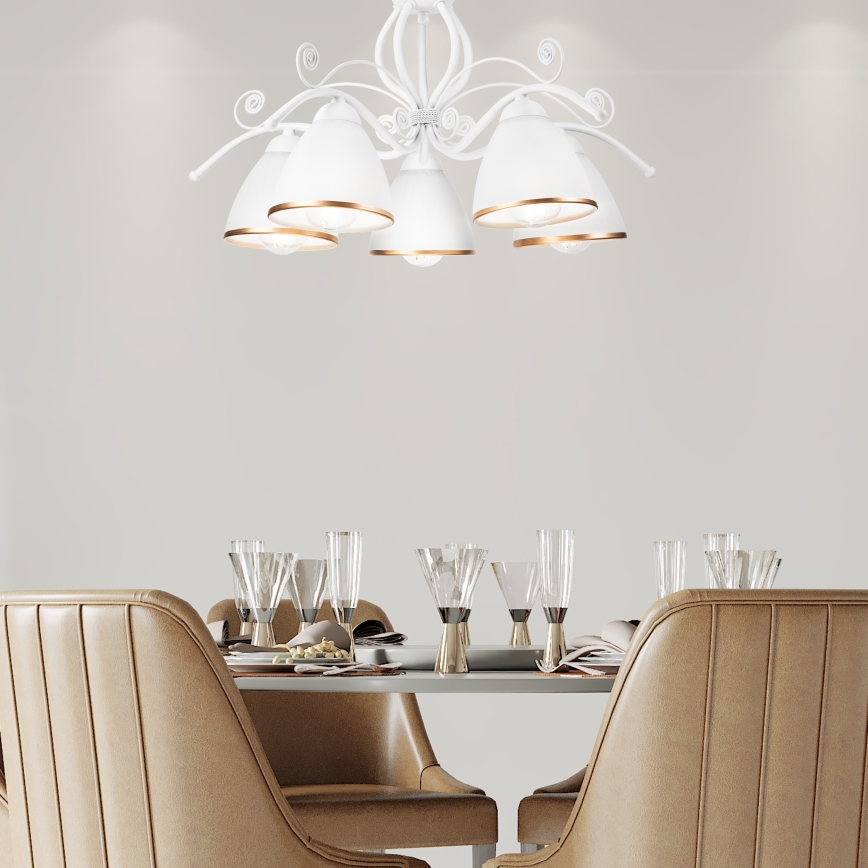 Biela luster s piatimi tienidlami s bronzovými okrajmi visí nad jedálenským stolom. Stôl je prestretý pre hostí s pohármi a taniermi. Stoličky sú kožené, béžovej farby.