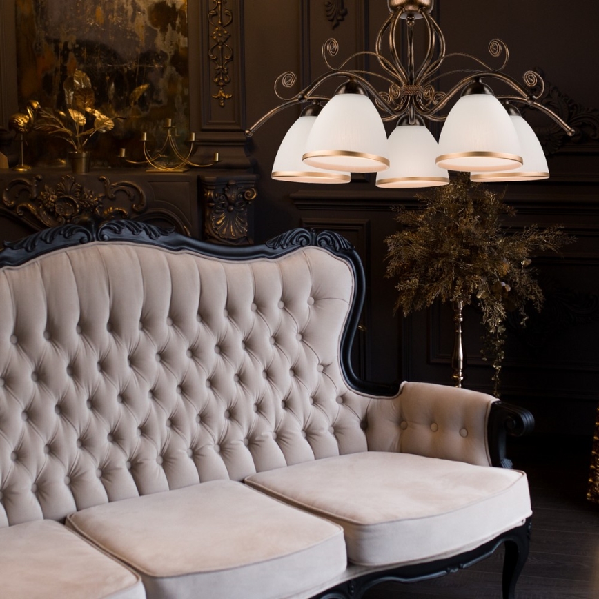 Čalúnená pohovka s čalúnením s prešívaním stojí v tmavej miestnosti. Nad ňou visí luster s viacerými tienidlami. V pozadí je tmavá stena s dekoratívnymi prvkami.