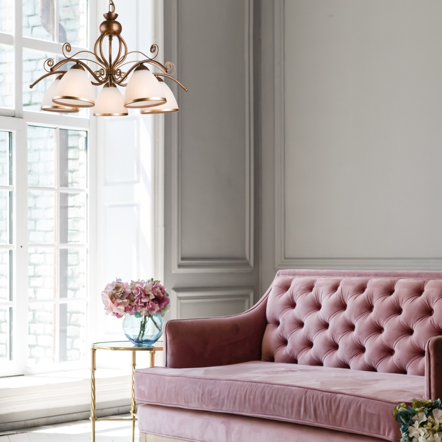 Kožený gauč s vankúšmi sa nachádza v interiéri. Nad ním visí lustre s piatimi tienidlami. Na stene za gaučom sú obrazy.